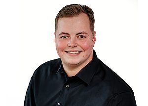 Freundliches Business-Porträt einer Person mit kurzen Haaren und schwarzem Hemd vor weißem Hintergrund