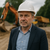 Bauleiter mit Schutzhelm auf Baustelle – Projektleitung im Bauwesen mit Bagger und Lkw im Hintergrund
