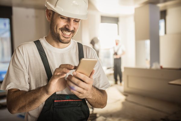 Mit einem Smartphone füllt ein Mann auf der Baustelle ein Bautagebuch aus