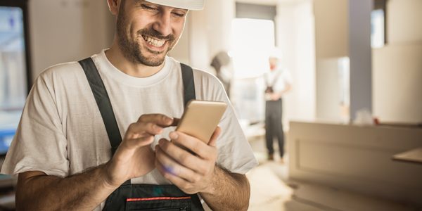 Mit einem Smartphone füllt ein Mann auf der Baustelle ein Bautagebuch aus