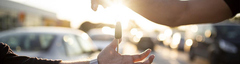 Fahrzeugübergabe mit Schlüsselübergabe bei Sonnenuntergang auf einem Parkplatz