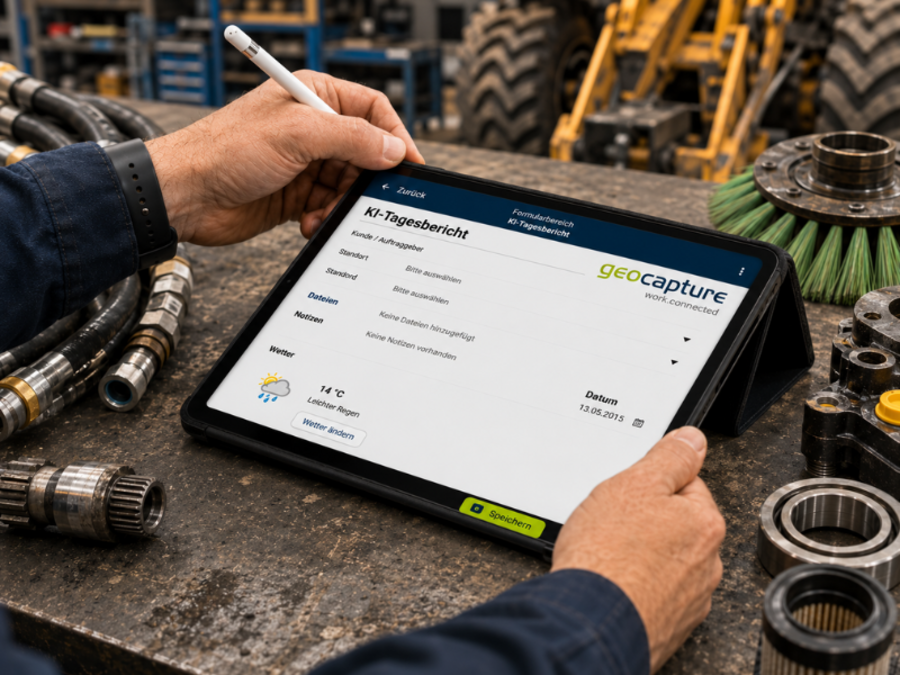 Ein Mitarbeiter bedient mit einem Eingabestift ein Tablet auf einer Werkbank. Auf dem Bildschirm ist eine geoCapture-KF-Tagesübersicht geöffnet; rundherum liegen Hydraulikschläuche, Lager, Maschinenteile und weitere Werkstattkomponenten.