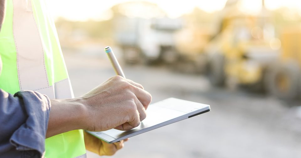 Auf einer Baustelle unterschreibt ein Mann auf einem Tablet ein digitales Bautagebuch