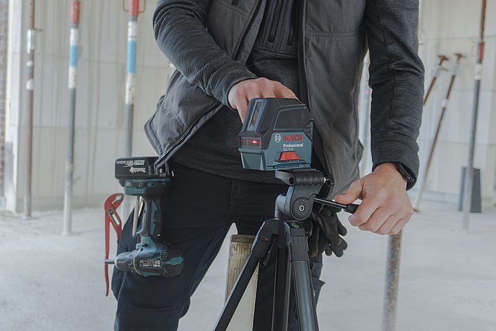 Handwerker richtet ein Laser-Messgerät auf einem Stativ im Rohbau ein.
